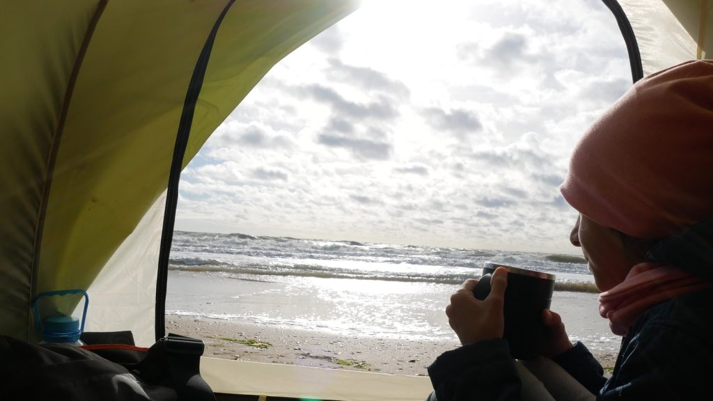 Tent on the beach. view from the tent on the sea. girl sitting in tent, drinking hot tea from thermo mug and looking at sea, all possible with lifestyle loans.