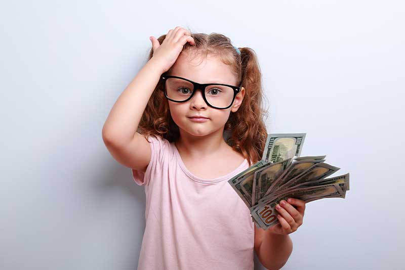 child holding money and scratching her head, showing she doesn't have a strong kids financial literacy