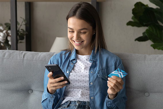 a young woman holding a DEXSTA card and looking at her share draft account on her cell phone.