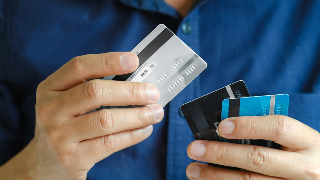 Mans hand holding credit cards and debit cards for a blog about pros and cons of debit cards vs credit cards